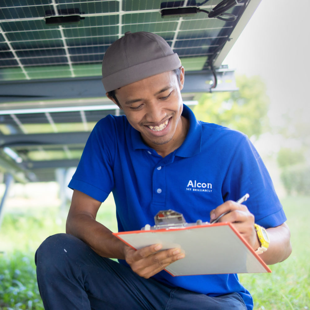 A man under some solar panels in a blue Alcon shirt, taking notes.